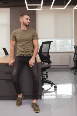 Modern ofisteki çalışma masasında oturan yakışıklı bir erkek girişimcinin dikey portresi.