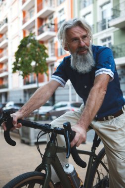 Şehrin sokaklarında bisiklet süren gri saçlı bir adamın dikey alçak açılı görüntüsü.