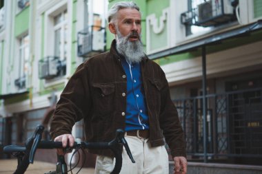Yakışıklı, sakallı, stil sahibi, gri saçlı, bisiklet süren bir adam.