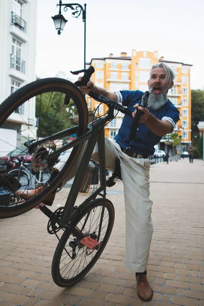 Yaşlı, sakallı, kır saçlı ve bisikletle sokakta eğlenen yaşlı bir adamın tam boy dikey görüntüsü.