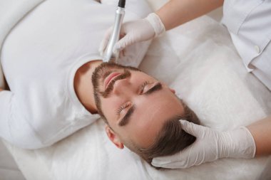 Tanımlanamayan kozmetolojist, erkek müşterinin boynunda rf-lift teçhizatı kullanıyor.