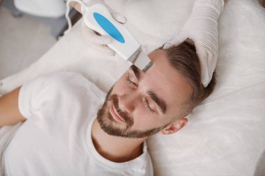 Çekici sakallı adam kozmetikçi tarafından ultrason temizliği yaptırıyor.