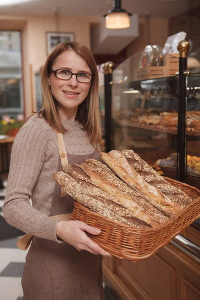 Kameraya gülümseyen, kafesinde ekmek sepeti taşıyan mutlu bir fırıncının dikey portresi.