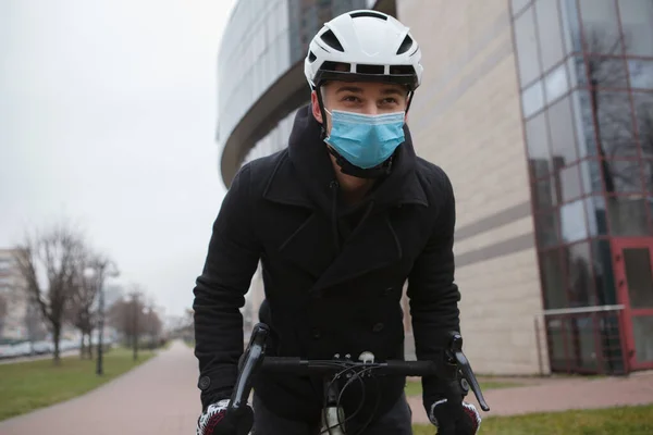 Low angle shot of a man wearing medical face mask and protective cycling helmet while riding bicycle