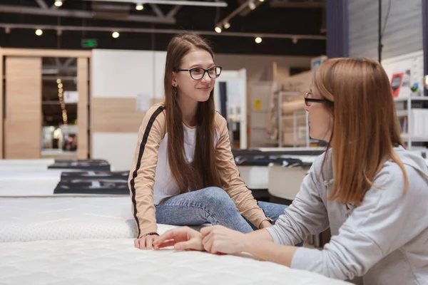 stock image Happy teen girl talking to her mom while choosing new orthopedic mattress to buy