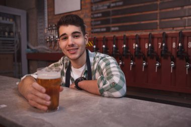 Genç barmen neşeyle gülümsüyor, bardak servis ediyor. Lezzetli bira, fotokopi odası.