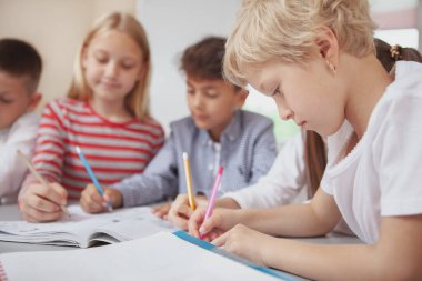 Küçük mutlu çocuklar konsantre oluyor, resim dersinde birlikte resim çiziyorlar. Güzel okul çocukları birlikte yaratıcı bir sanat projesi üzerinde çalışıyorlar, renkli kalemlerle çizim yapıyorlar.