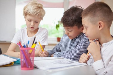 Çocukluk, iletişim konsepti. Sanat projesinde birlikte çalışan bir grup küçük çocuk. İki okul çocuğu ve resim çizen bir kız.