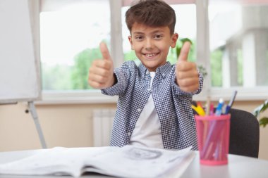 Mutlu genç çocuk ödevlerini yaparken mutlu bir şekilde gülümsüyor. Sevimli okul çocuğu ders çalışmaktan hoşlanıyor. Eğitim, güven, çocukluk kavramı