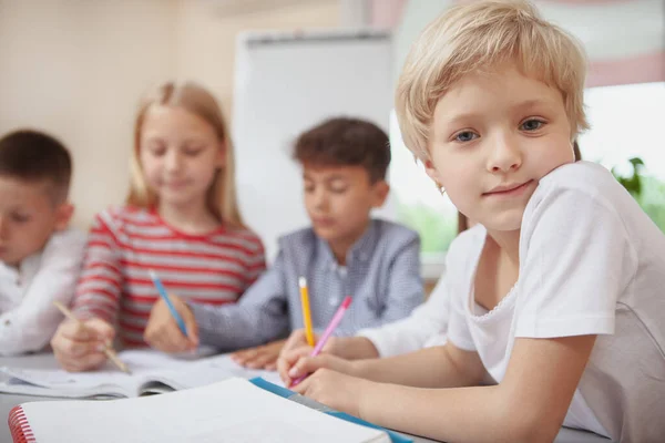 Charming little blond haired girl looking to the camera during art class, copy space. Adorable schoolgirl enjoying drawing at elementary school lesson