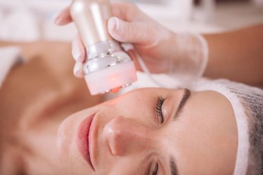 Profesyonel bir dermatolog tarafından kadın bir müşterinin rf-lift prosedürü uygulanırken görüntülenmiş. Çekici kadın yüz bakımı görüyor.