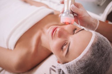Güzel, rahat bir kadın güzellik salonunda rf-lift seansında eğleniyor. Profesyonel kozmetik uzmanı kadın müşteri için cilt sıkma işlemi yapıyor.
