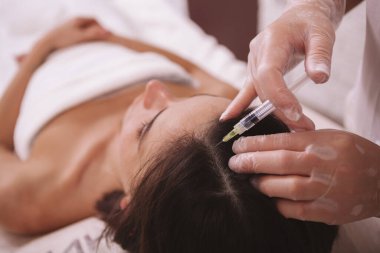 Güzellik kliniğinde tanınmayan bir kadın saç bakım yaptırıyor. Kadın bir hastanın kafasına kellik önleyici enjeksiyon yapan profesyonel bir güzellik uzmanı.