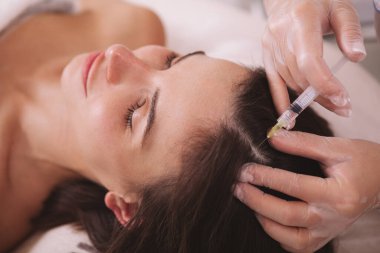 Kafa derisine vitamin iğnesi yaptıran bir kadın. Profesyonel dermatolog tarafından saç dökülmesi tedavisi gören bir kadın hasta.