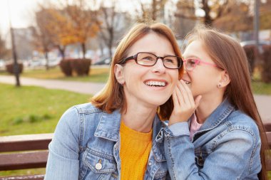 Olgun bir kadın gülerken kızı ona komik bir şey fısıldıyor.
