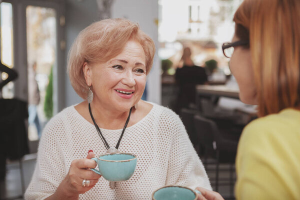 Милая пожилая женщина радостно улыбается, болтает со своей взрослой дочерью в кафе