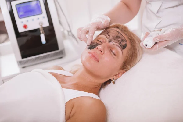 Profesjonalny Kosmetolog Stosujący Czarny Nanogel Twarz Dojrzałej Klientki Kobieta Otrzymywać — Zdjęcie stockowe