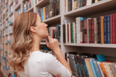 Kitap raflarına dikkatlice bakan bir kadının arka plan görüntüsü, boşluğu kopyala