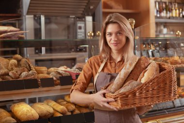 Fırınında çalışan ve bir sepet dolusu taze pişmiş ekmek taşıyan mutlu, olgun bayan girişimci.