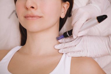 Cropped shot of unrecognizable woman receiving microinjections in her neck skin. Cosmetologist using dermapen on female client clipart