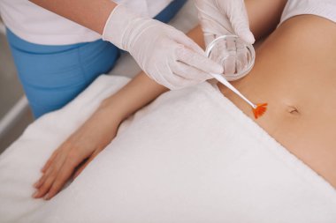 Profesyonel bir kozmetikçinin, kadın bir müşterinin göbek derisini nemlendirici iğnesi.