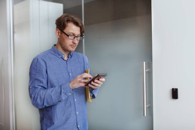 Yetişkin bir girişimci ofis koridorunda yürürken akıllı telefon kullanır.