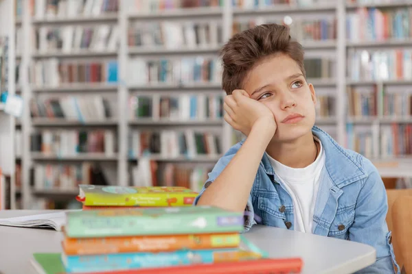 すべての彼の本の前に図書館に一人で座って 離れて見て悲しい少年 — ストック写真