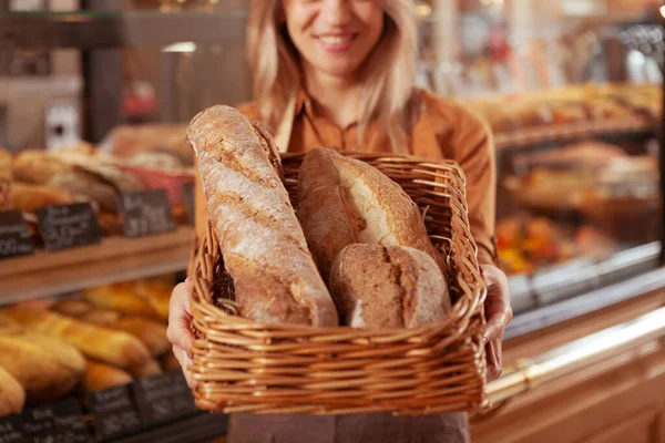 カメラにおいしいオーガニックパンのバスケットを持っている幸せな女性のパン屋 彼女のパン屋で働いている — ストック写真