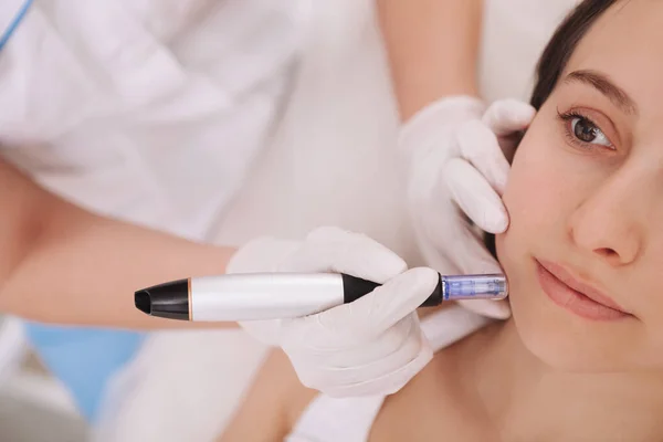 Profesyonel dermatolog tarafından yüz terapisi gören genç bir kadının görüntüsü.