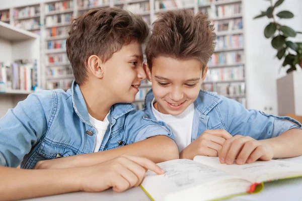図書館で一緒に勉強しながら 彼の双子の弟に静かにささやく陽気な若い男の子 — ストック写真