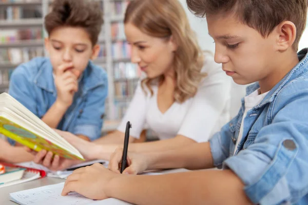 彼の教科書に書いてある若い男の子の終わり 彼の母親と双子の弟はバックグラウンドで本を読んでいます — ストック写真