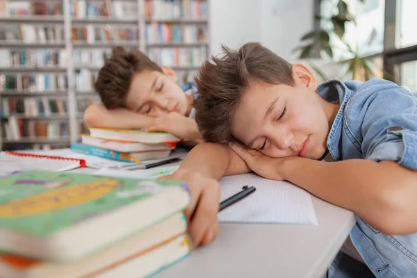 若い双子の男の子がテリ本の上で寝て 勉強した後に疲れを感じている 疲れた子供たちが図書館で眠っている — ストック写真
