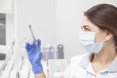 Close up of a female doctor wearing medical face mask, looking at the syringe she is holding