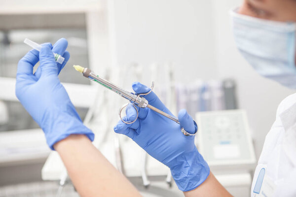 Cropped close up of a female dentist preparing anesthesia syringe for patient