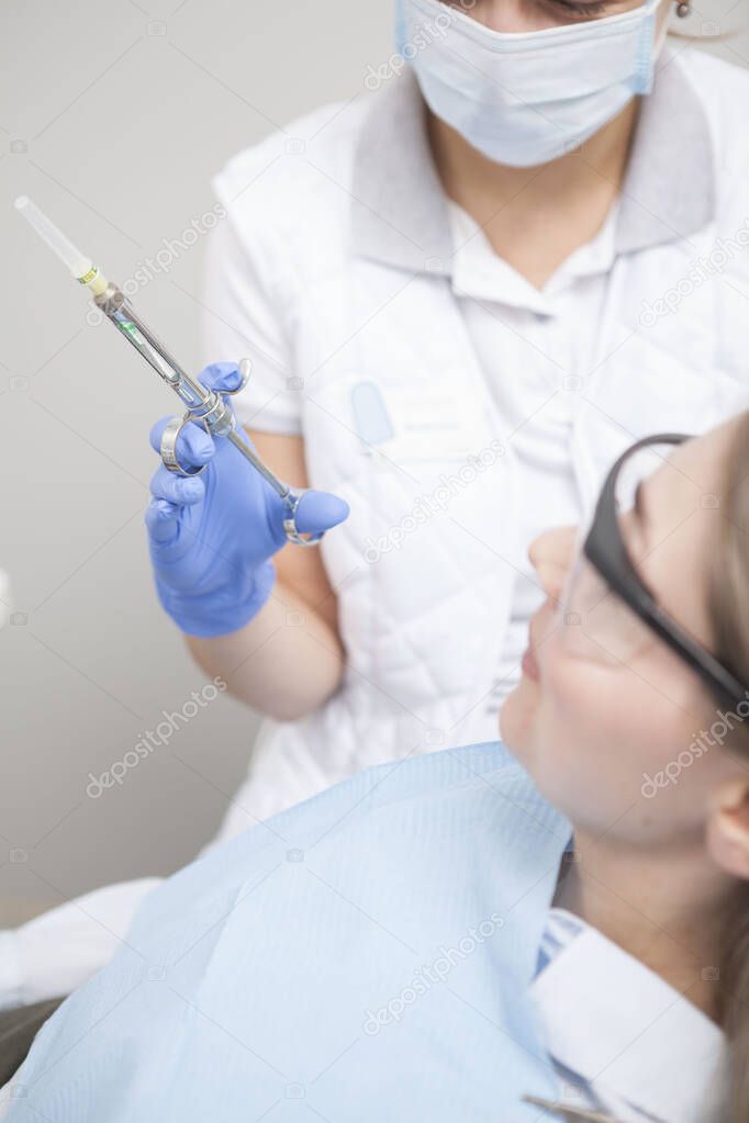 Vertical shot of female dentist holding syringe with anesthetic, working with patient