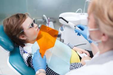 Dişçisinin diş tedavisi sırasında koruyucu gözlük takan genç bir çocuk.