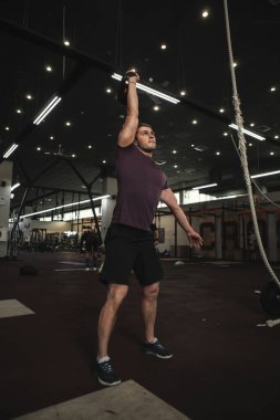 Spor salonunda kettlebell ile egzersiz yapan kaslı bir gencin tam boy çekimi.