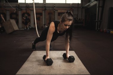 Dambıllarla şınav çeken bayan sporcu.