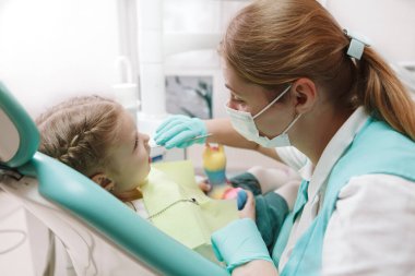 Childrens dentist working at her clinic, examining teeth of little girl