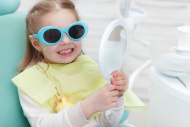 Close up of a cute little girl wearing protective glasses sitting in dental chair