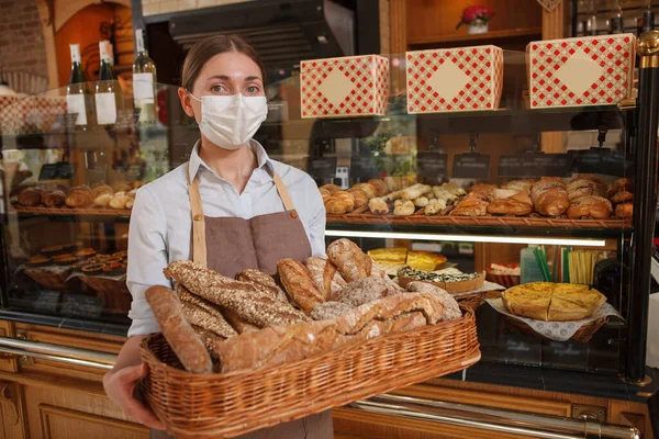 コロナウイルス検疫中に彼女のパン屋でおいしいパンを販売しているプロのパン屋 顔マスクを身に着けています — ストック写真