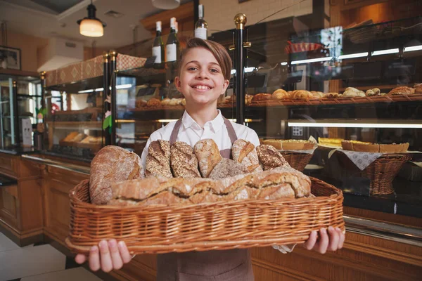 幸せな若い男の子は新鮮なパンでいっぱいのバスケットを持っていて 家族のパン屋で両親を助けています — ストック写真