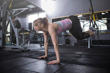 Atletik kadın trx sistem eğitmeni üzerinde kalas egzersizi yapıyor.