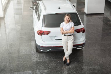 Araba galerisindeki yeni cipinin yanında duran bir kadın sürücünün en iyi görüntüsü.