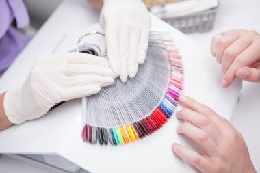 Profesyonel manikürcü müşterisine tırnak jeli renk paletini gösteriyor