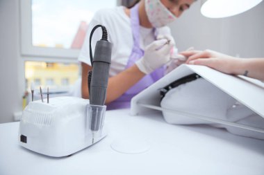 Tırnak matkabı üzerine seçici odaklanma, arka plan üzerinde çalışan profesyonel manikürcü