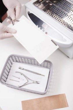 Manikür aletlerini sterilize etmek ve dezenfekte etmek için kuru ısı makinesi kullanan manikürcünün dikey üst görüntüsü