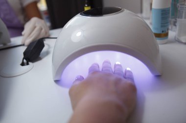 Manikürlü bir el yaklaştı. Manikürcüdeki UV lambasında kurutuluyor.