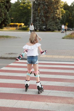 Yaya geçidinde paten kayan genç bir kızın dikey dikey görüntüsü.
