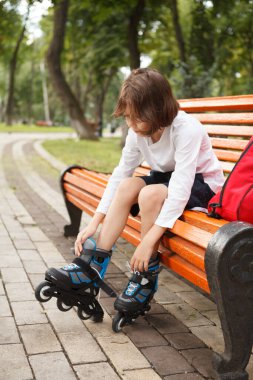 Park bankında oturan, paten takan bir çocuğun dikey uzun pozu.